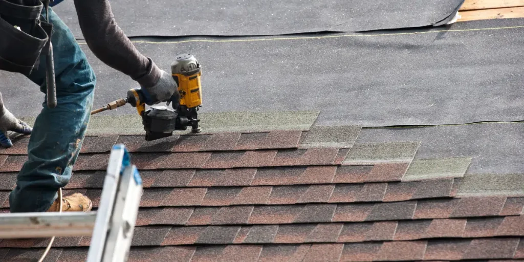 Roofer installing new shingles with a nail gun