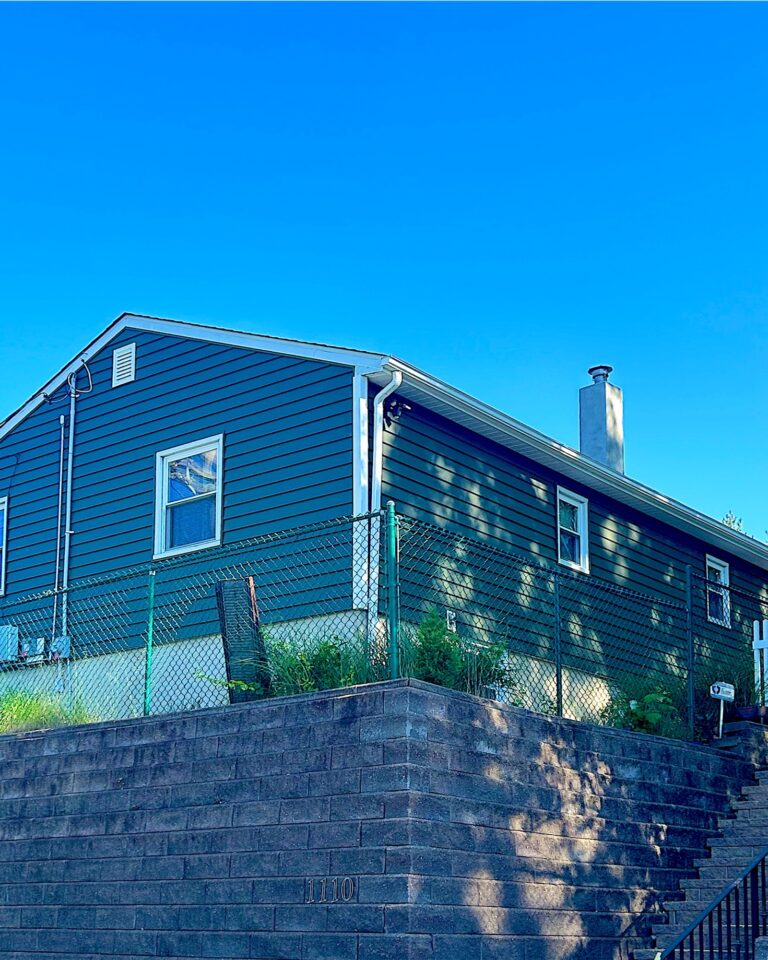 Ranch home with new green vinyl siding above a stone retaining wall in Highlands, NJ