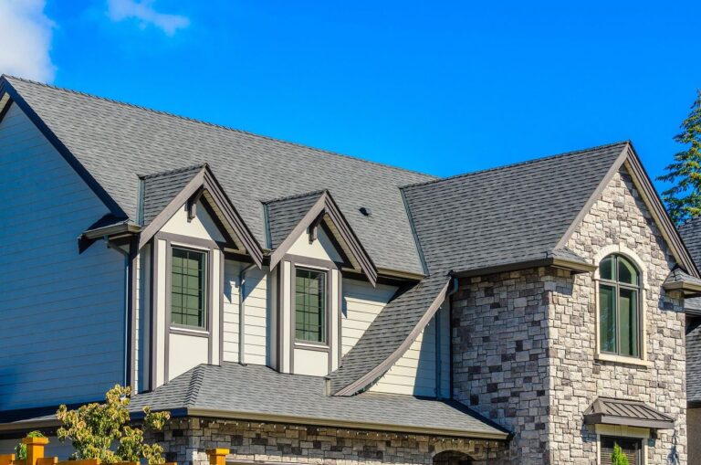 Gray shingle roof on a home with blue siding and stone veneer